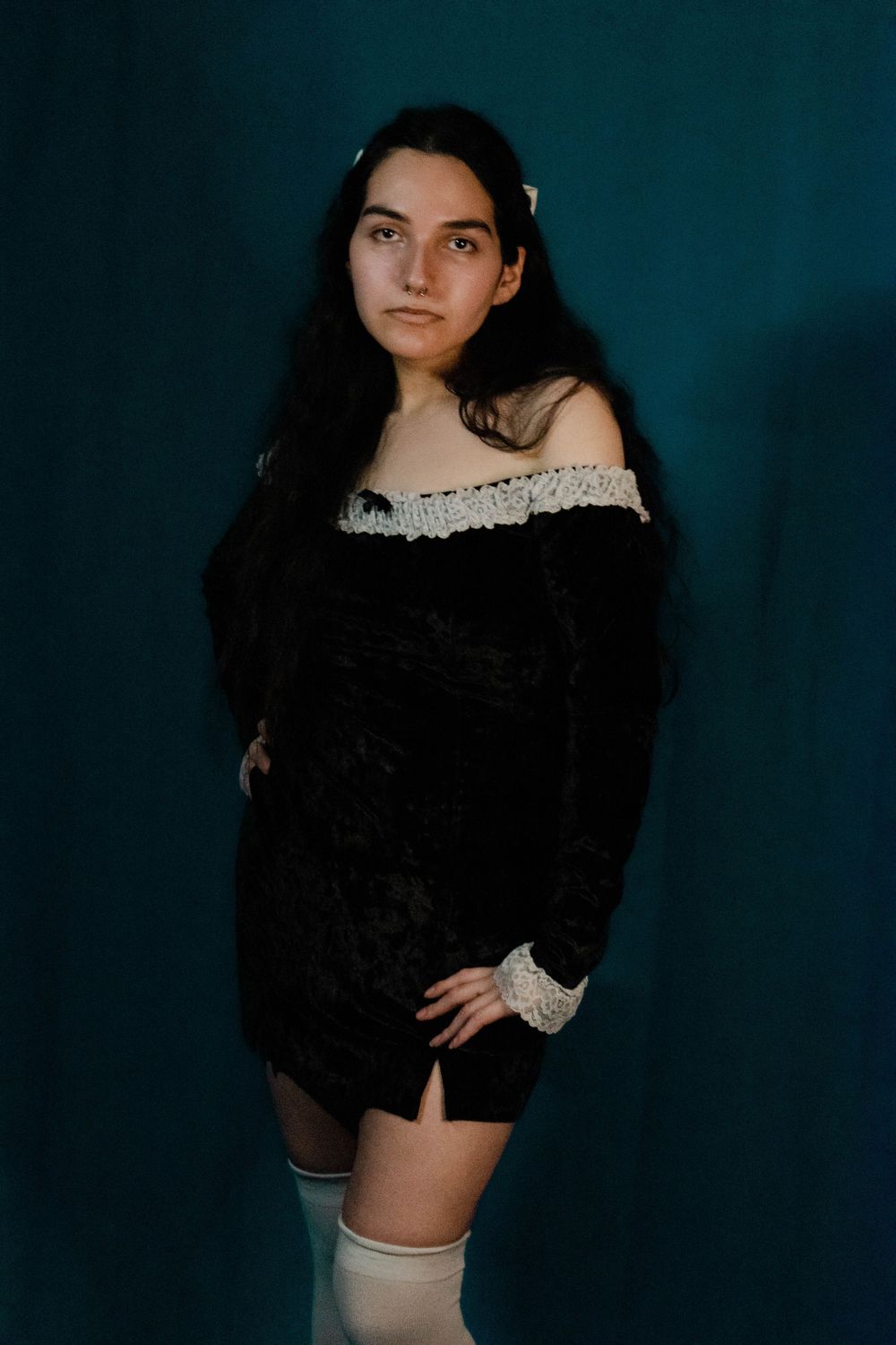 Dark velvet dress with lace trim and thigh high socks against teal backdrop.