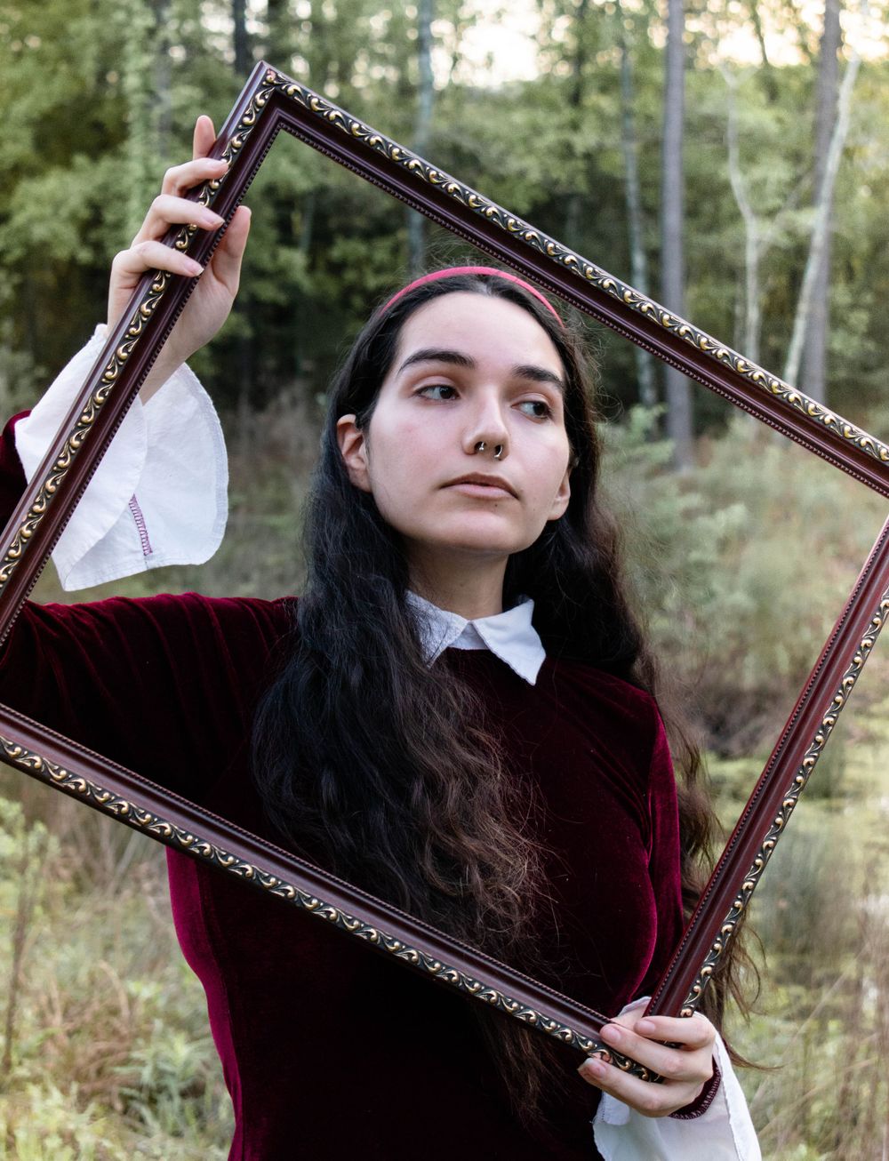 Creative portrait with antique frame in forest setting.