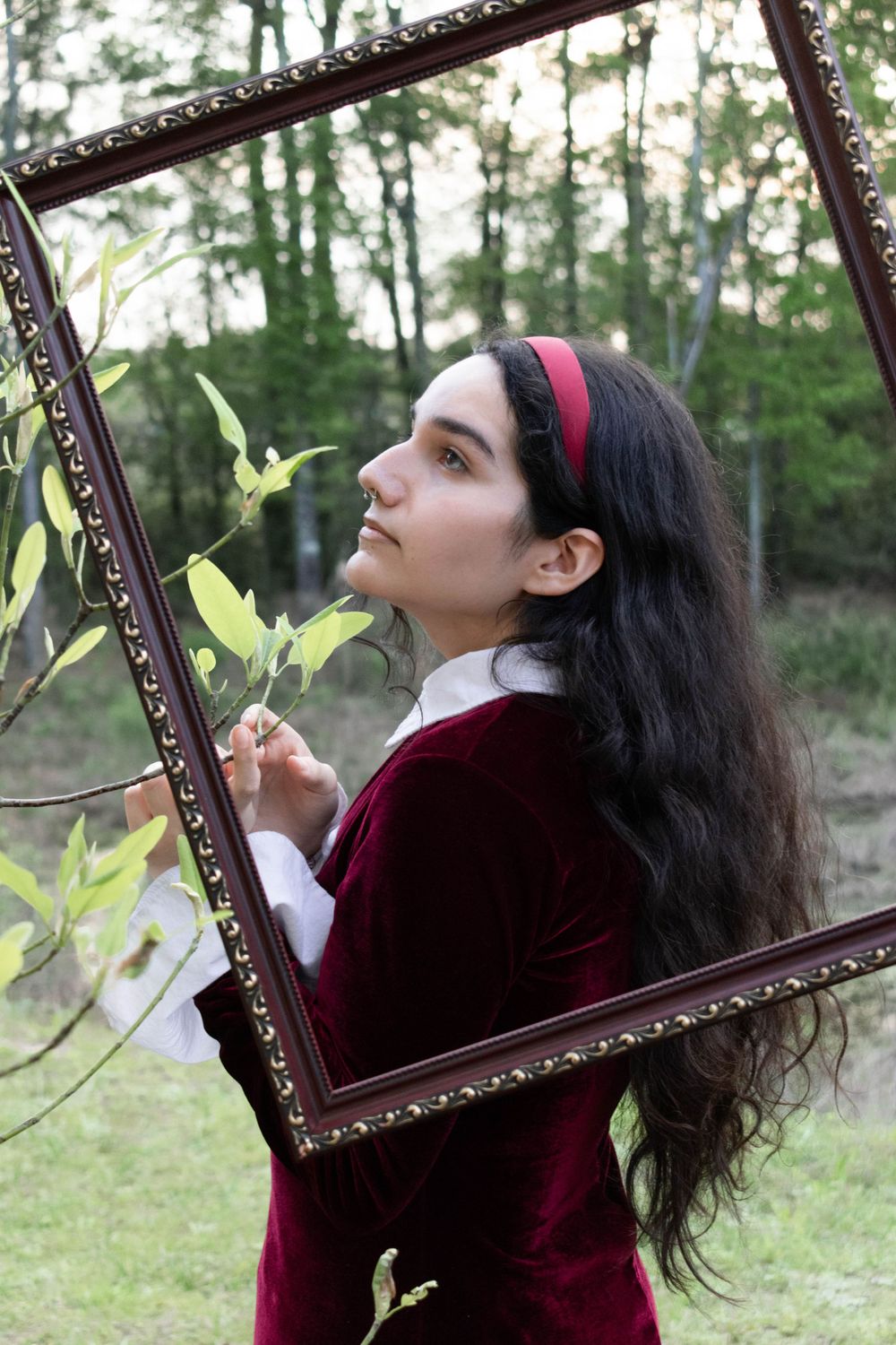 Artistic outdoor portrait with vintage frame and velvet dress among trees.
