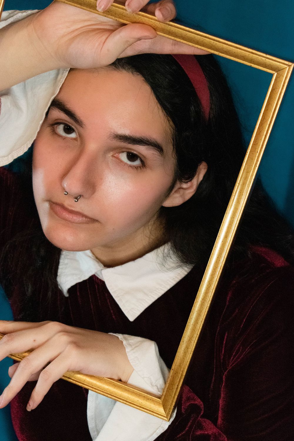 Creative portrait with gold frame, burgundy velvet top and white collar against teal background.