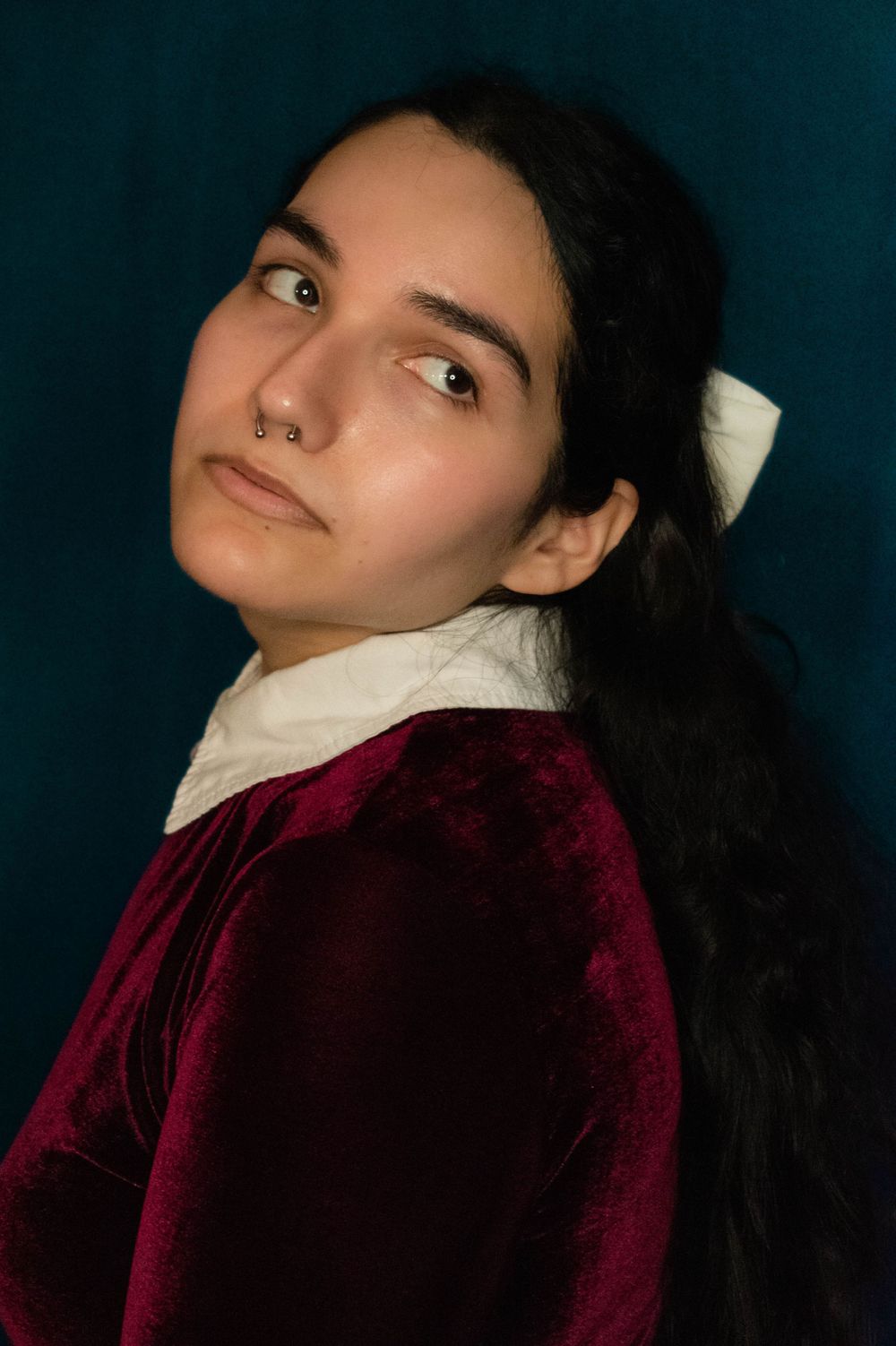 Dramatic portrait in burgundy velvet and white collar against dark teal backdrop.