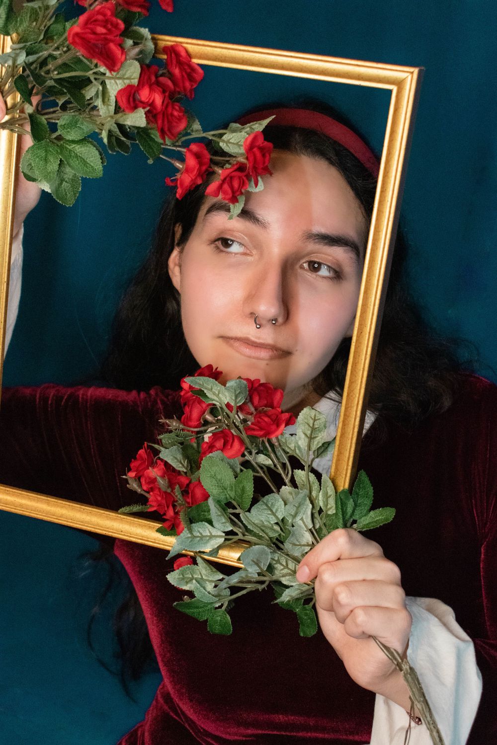 Vintage-styled portrait with red roses and gold frame against teal background.