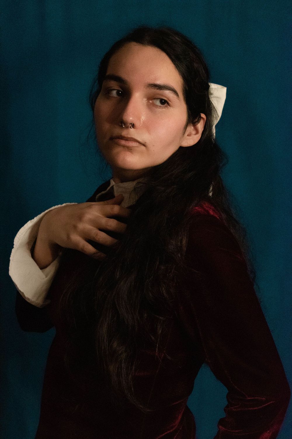 Dramatic portrait featuring velvet dress and white collar against deep blue backdrop.