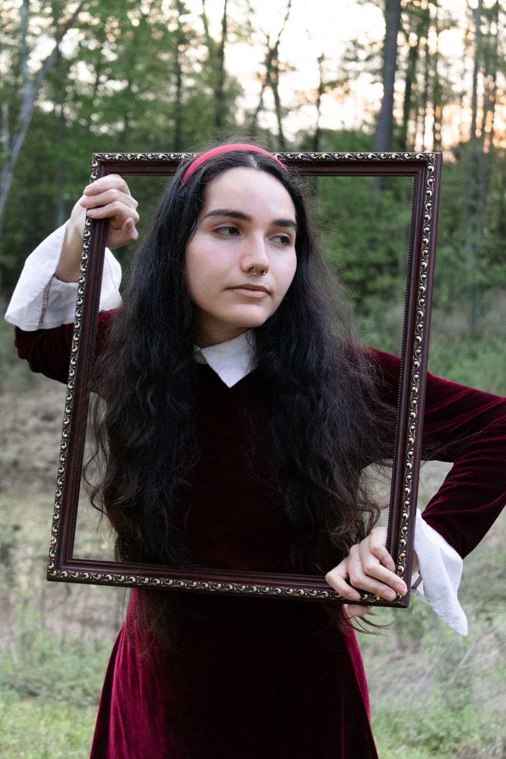 Artistic portrait with ornate frame in outdoor setting with forest backdrop.