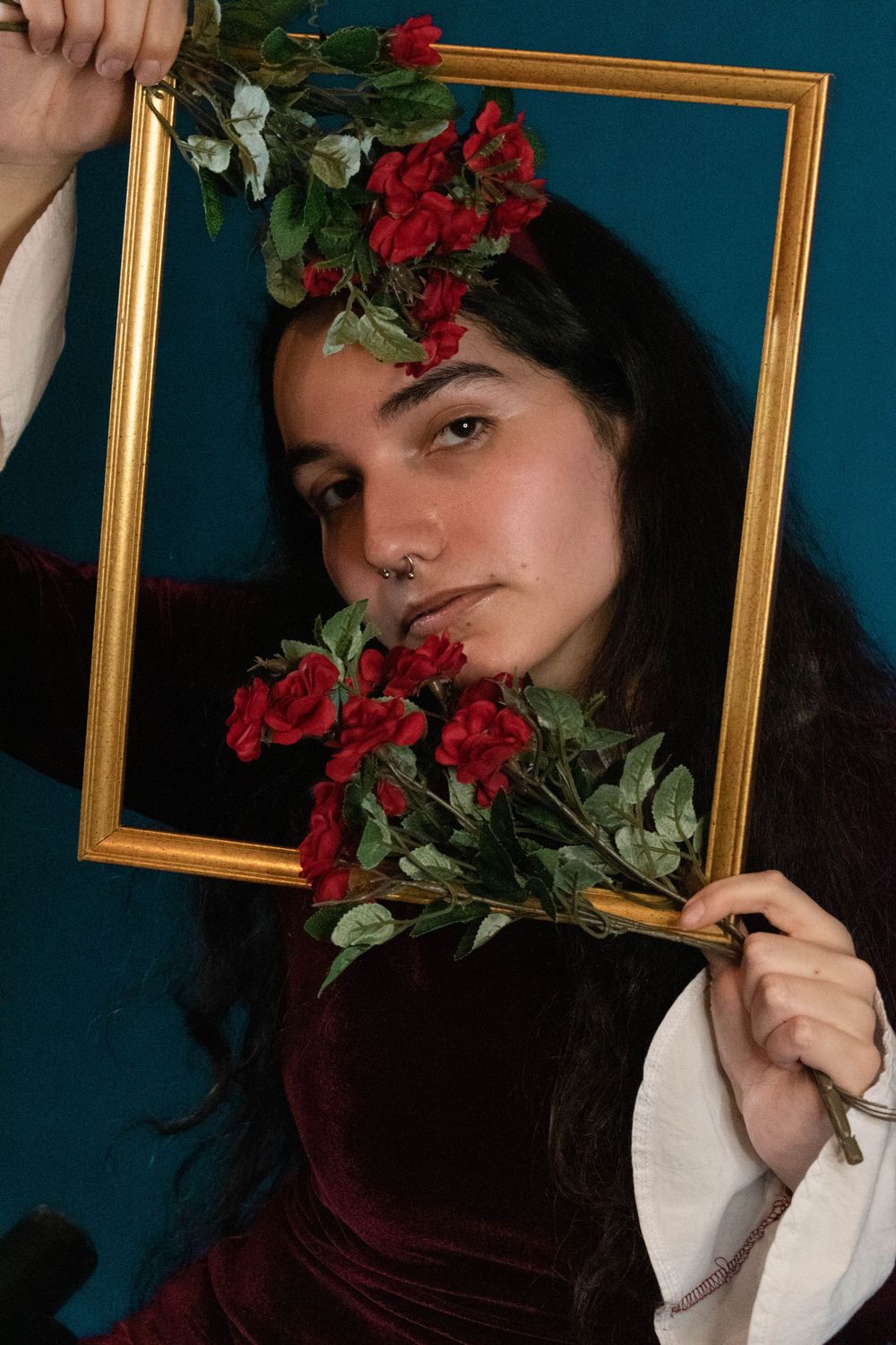 Artistic portrait with gold frame decorated with red roses against teal background.