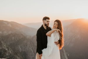 Couple embracing on mountain overlook during golden hour with dramatic valley views.