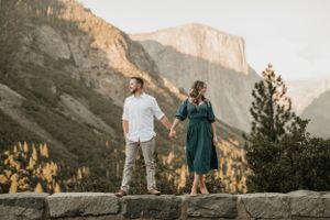 A couple stands on a rocky ledge with majestic Yosemite mountains in the background.