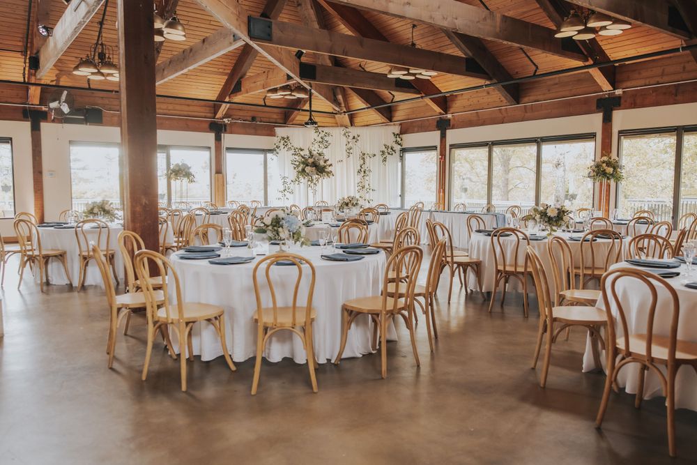 Spacious wooden beam reception hall with round tables and natural lighting.