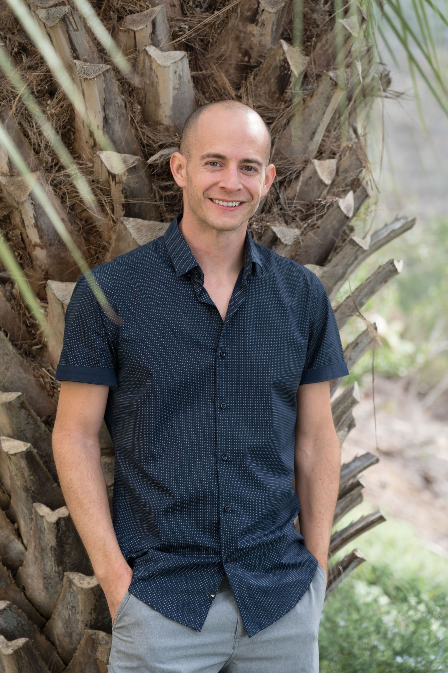 Wedding, engagement and family portrait photographer, Kevin Young, poses in front of a palm tree.