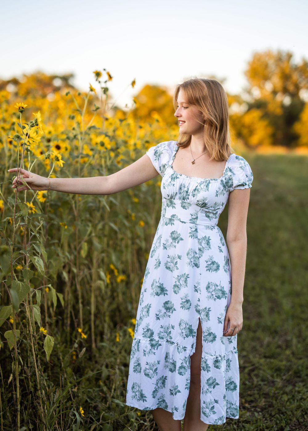 A dreamy outdoor portrait with someone reaching toward sunflowers in a floral dress at sunset.