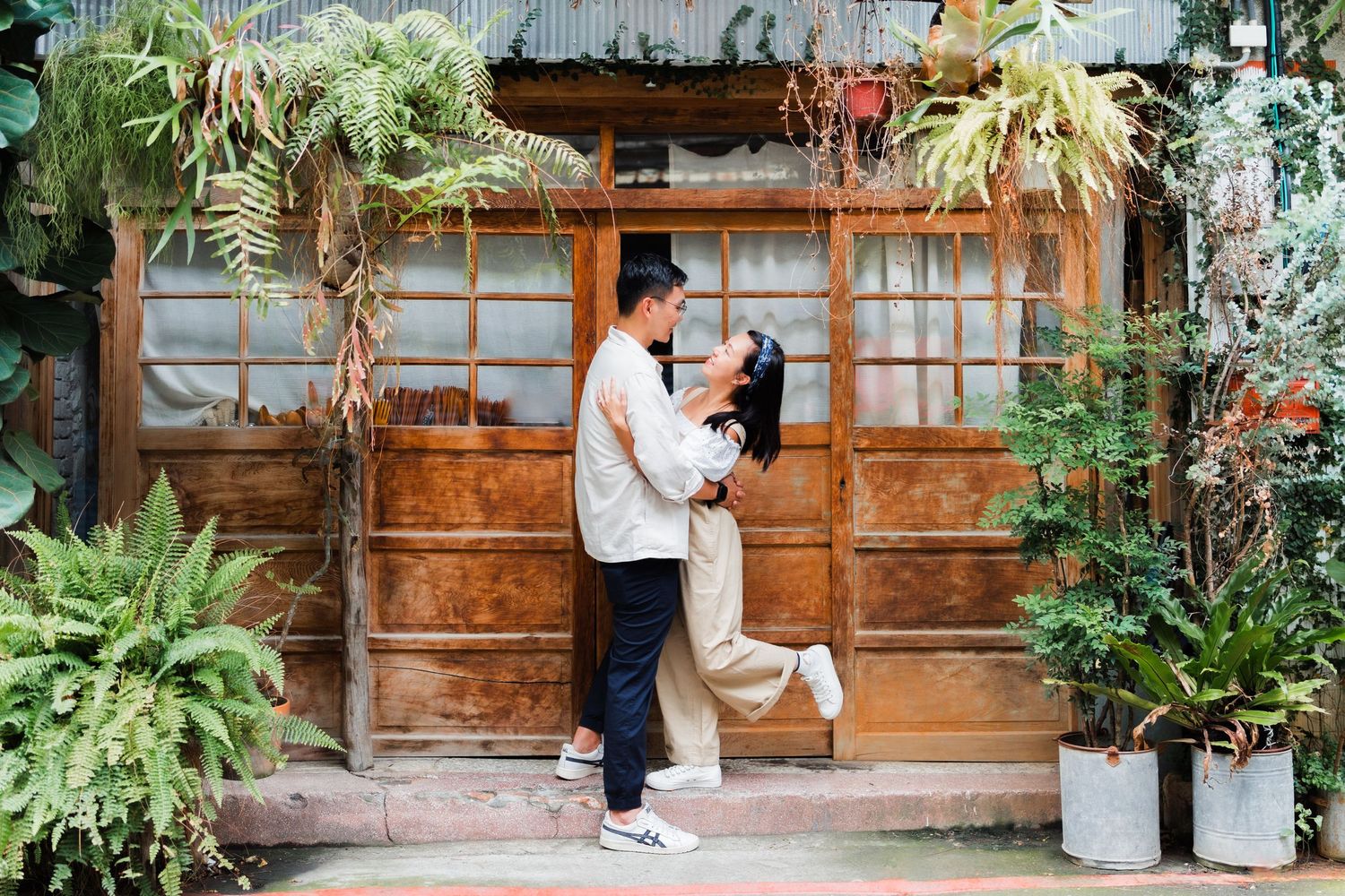 A romantic moment captured against a rustic wooden backdrop decorated with hanging plants.