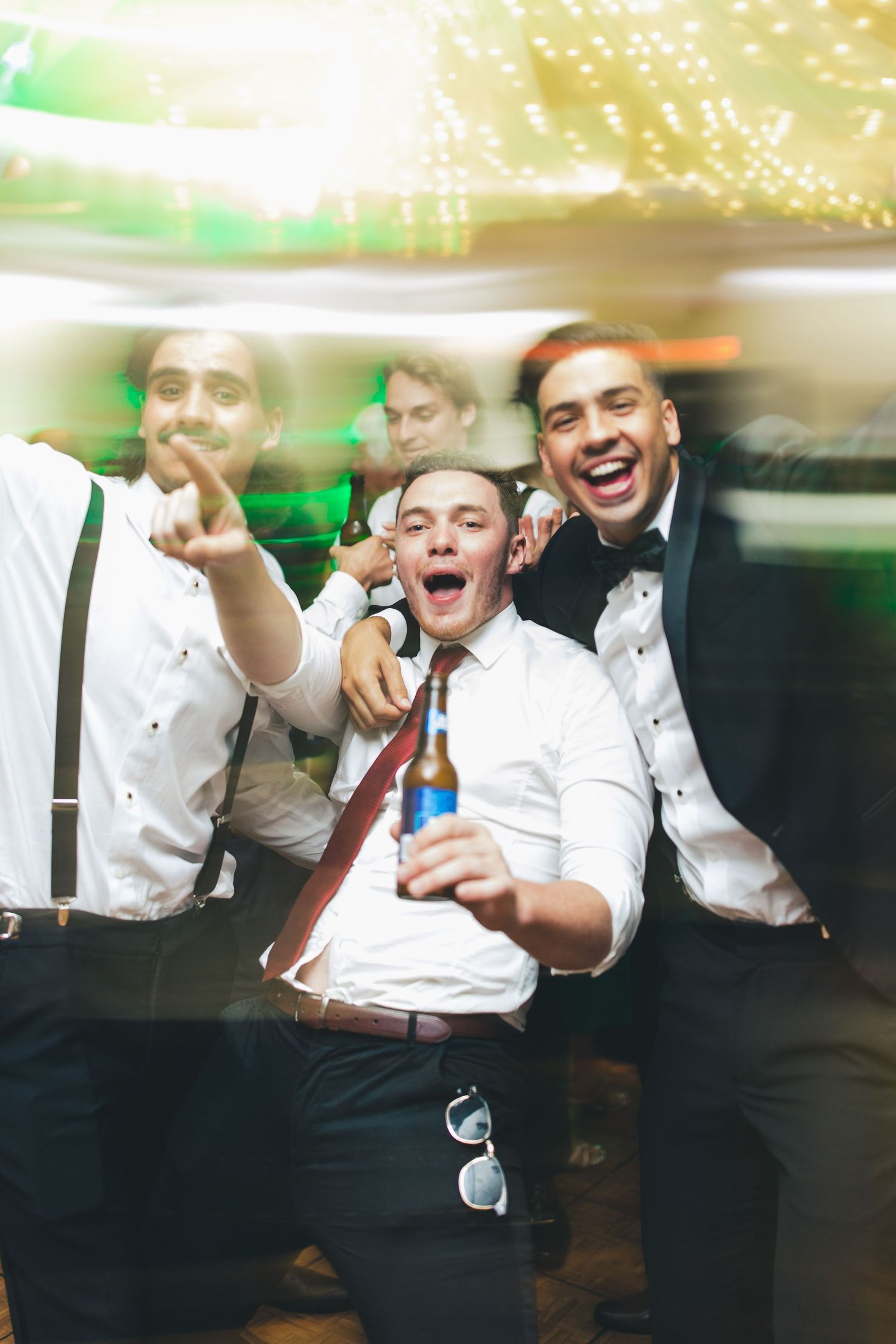 Groomsmen in formal wear celebrate at reception with drinks and laughter.