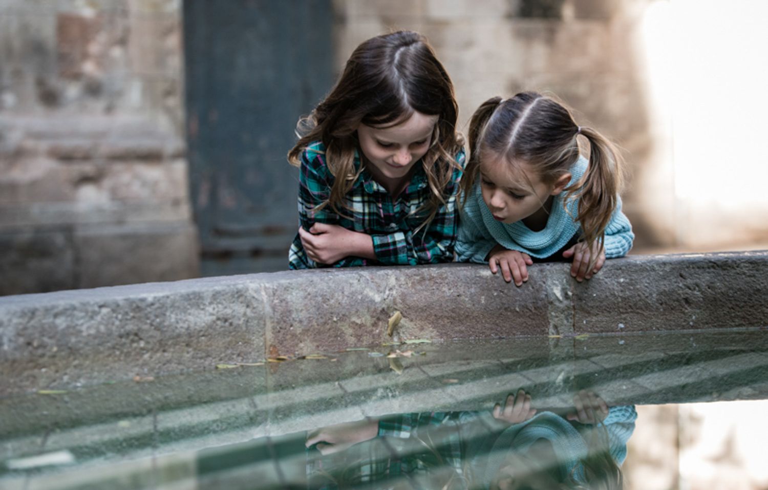 Two sisters look into a fountain on a photoshoot in the old quarter of Barcelona