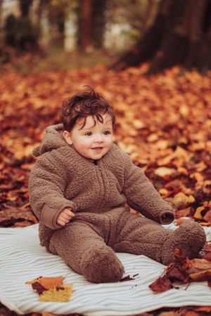 Little boy sat in the autumnal leaves, wearing a fluffy onesie suit