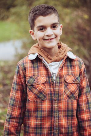 Little boy wearing autumnal colours, smiling at the camera.
