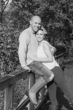 Black and white, man sat on a bridge, wife is leaning in and hugging him,