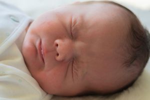 A close up of a newborn baby boy asleep. He is scrunching his eyes up.