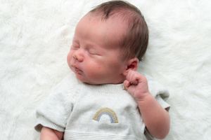A newborn baby boy asleep on a fluffy blanket. He has his hand up in the air.