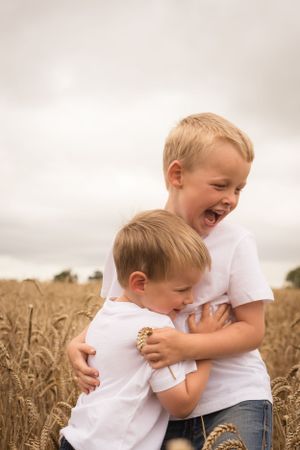 Two young brothers play fighting in a wheat field. They both have big smiles and laughing.