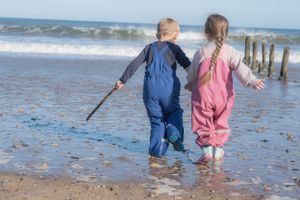 Little boy and girl holding hands and running along the beach, little boy holding a stick.