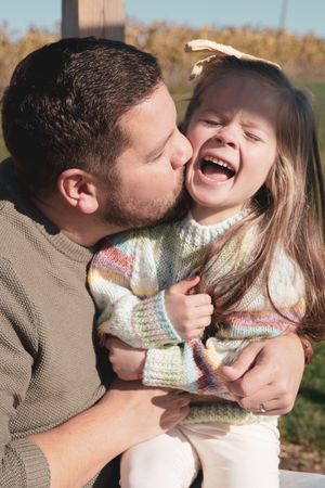 Young dad cuddling little girl, making her laugh and kissing her cheek.