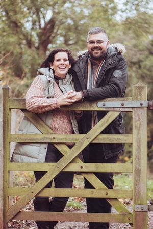 Couple leaning over a gate, holding hands and cuddling, smiling at the camera.