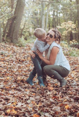 Mum crouched down having a kiss from her son. Surrounded by lots of brown leaves.
