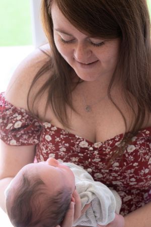 A new mum is holding her newborn baby, looking down at him and smiling.