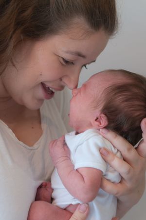 A mum is holding her newborn baby, they are nose to nose, mum has the biggest smile on her face.