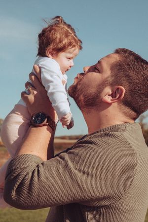 Young dad holding newborn baby up in the air and going to kiss her.