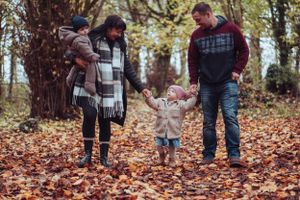Young family walking towards camera, all holding hands in the autumnal leaves.