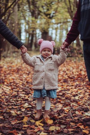 Little girl in the middle of her parents, holding their hands.