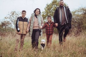 Family shot, all in a line, holding hands, smiling and walking towards the camera, dog in the shot as well