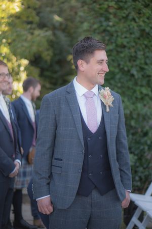 A groom watching his bride walking down the aisle towards him, with the biggest smile on his face.