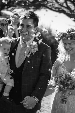 A black and white picture of a newlywed bride and groom walking through the confetti. Confetti flying everywhere.