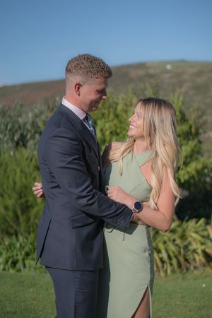 A young couple are in an embrace, they are looking into each others eyes and smiling.