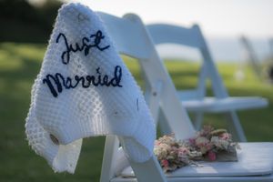 A Childs cardigan with 'Just married' embroidered on the back is draped on the edge of a chair. Two sets of button holes are on the chair