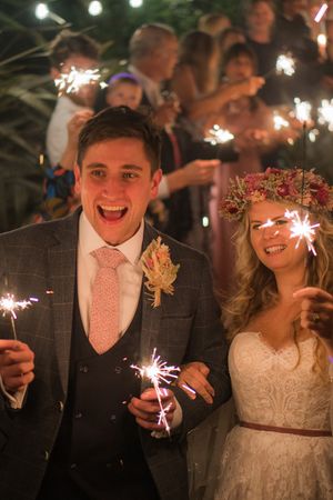 A newly wed couple holding sparklers, with all of their guest behind them also holding sparklers.