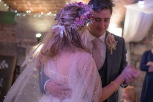 A newly wed couple during their first dance. They are embraced and she is looking at him, whilst he is looking down.
