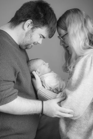 New parents holding their newborn baby in front of them, black and white.