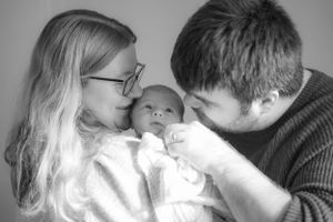 A black and white image of new parents cuddling their newborn baby girl.