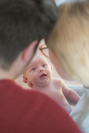 A new mum and dad have their heads resting together, there is a gap between them where the focus is on the newborn baby.