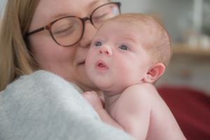 A new mum cuddling her newborn baby girl, looking at her as the baby looks over her shoulder.