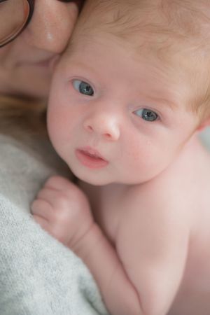 A newborn baby being cuddle by their mum, the baby is looking directly at the camera.