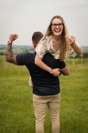Newly engaged couple, she is on his shoulder with her ring finger up, whilst he has his other arm out to the side cheering!