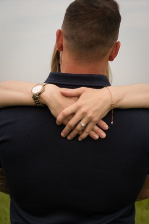 A newly engaged couple having a cuddle. Her arms are around his neck and he has his back to the camera. The focus is on the new ring!