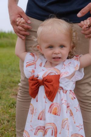 A close up of a little girl stood in front of her dads legs. They are holding hands.