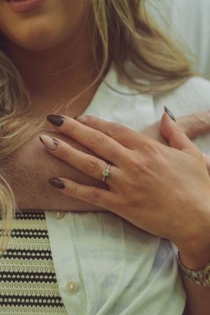 Couple are having a cuddle. She has her hand on top of his, on her shoulder. The focus is on the engagement ring.