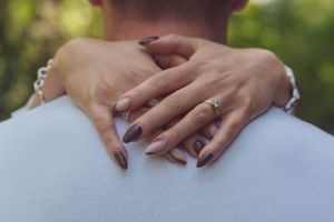 Hands of a female round males neck, the focus is on the engagement ring.