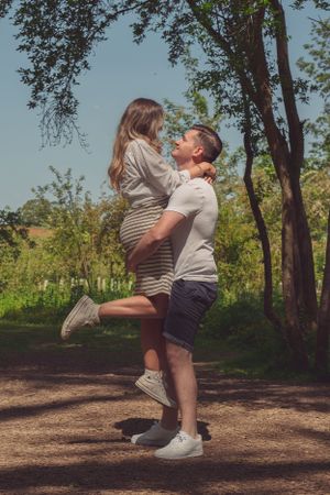 A young couple, the male is lifting up the female, whilst she is popping her leg. They are looking at each other with big smiles.